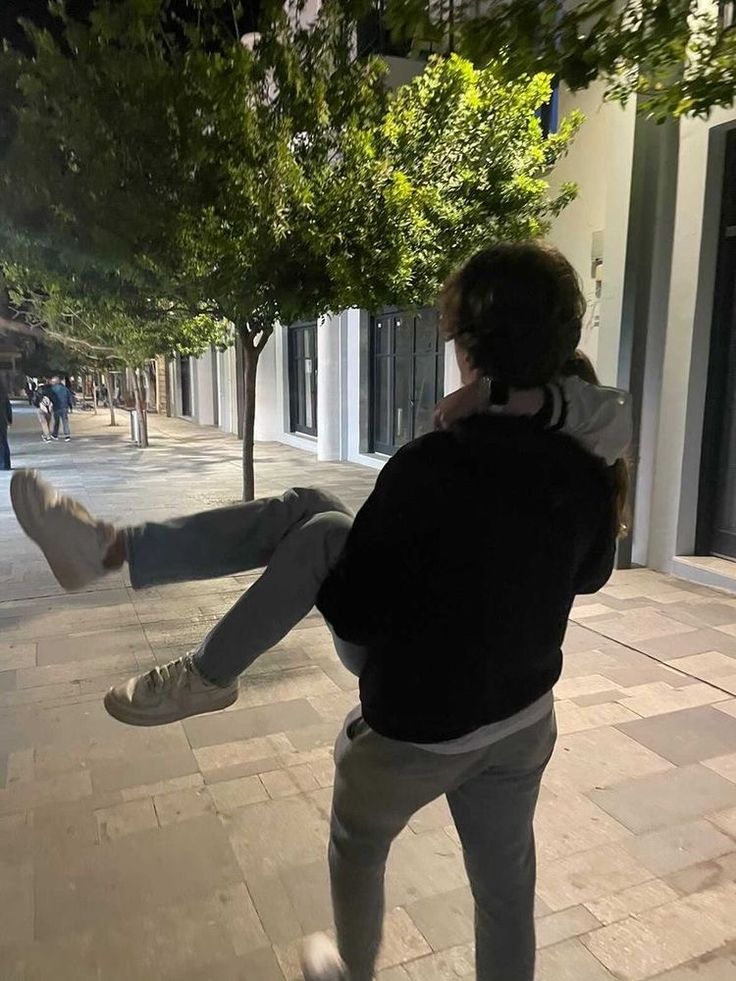 a man is dancing on the sidewalk with his feet in the air as he holds onto another person's leg