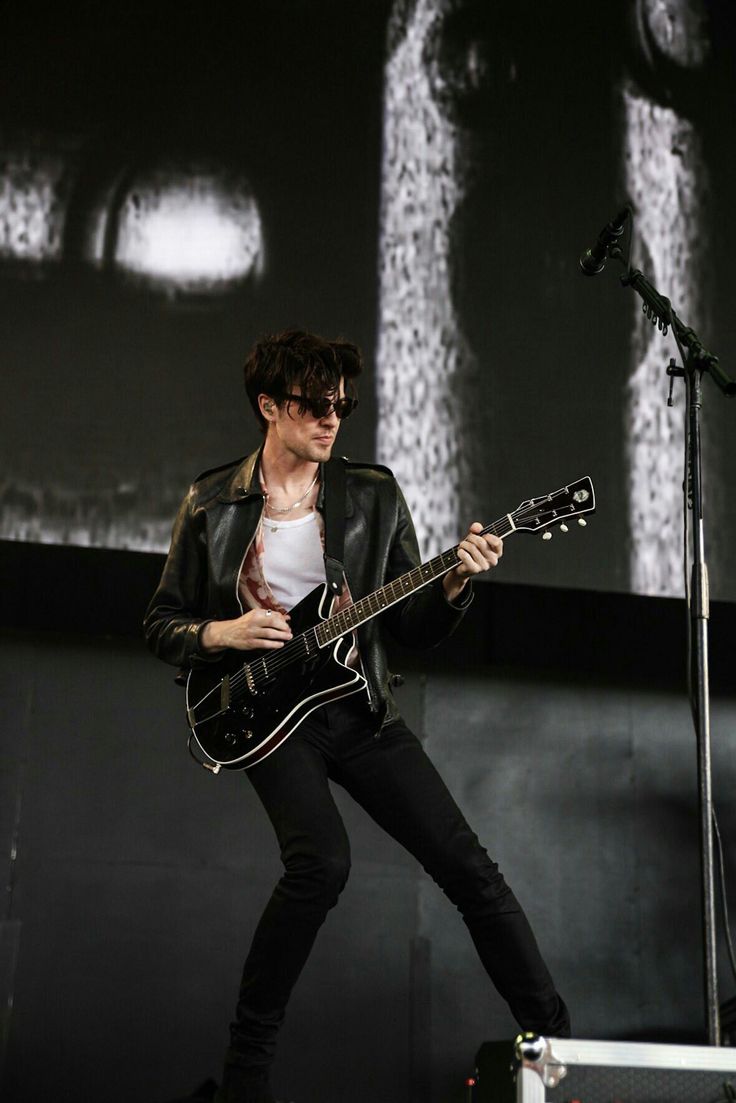 a young man playing guitar on stage at a music festival in front of a large screen