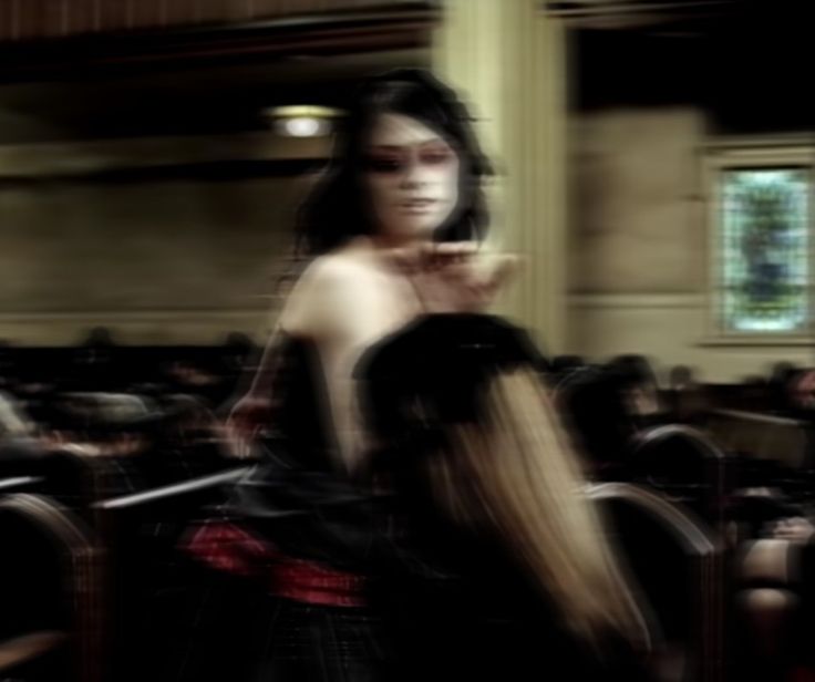 a blurry photo of a woman in a black dress with long hair standing in front of a room full of people