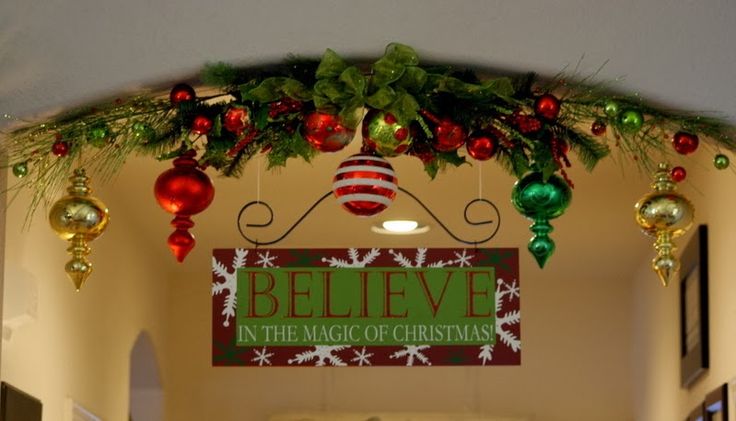 an archway decorated for christmas with ornaments and decorations hanging from it's sides, along with a sign that reads believe in the magic of christmas