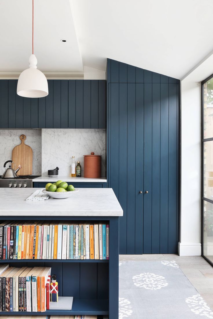 a kitchen with blue cabinets and bookshelves on the counter top in front of an open window