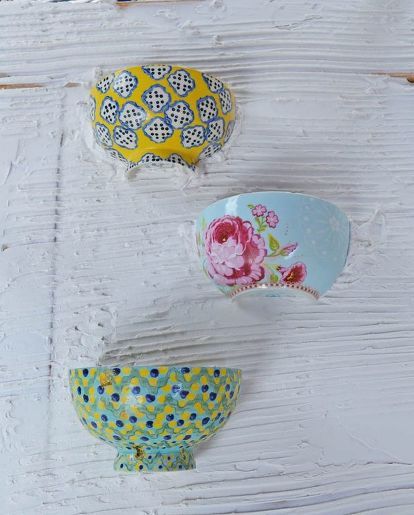 three colorful bowls are hanging on a white painted wood paneled wall, one is blue and the other has pink flowers