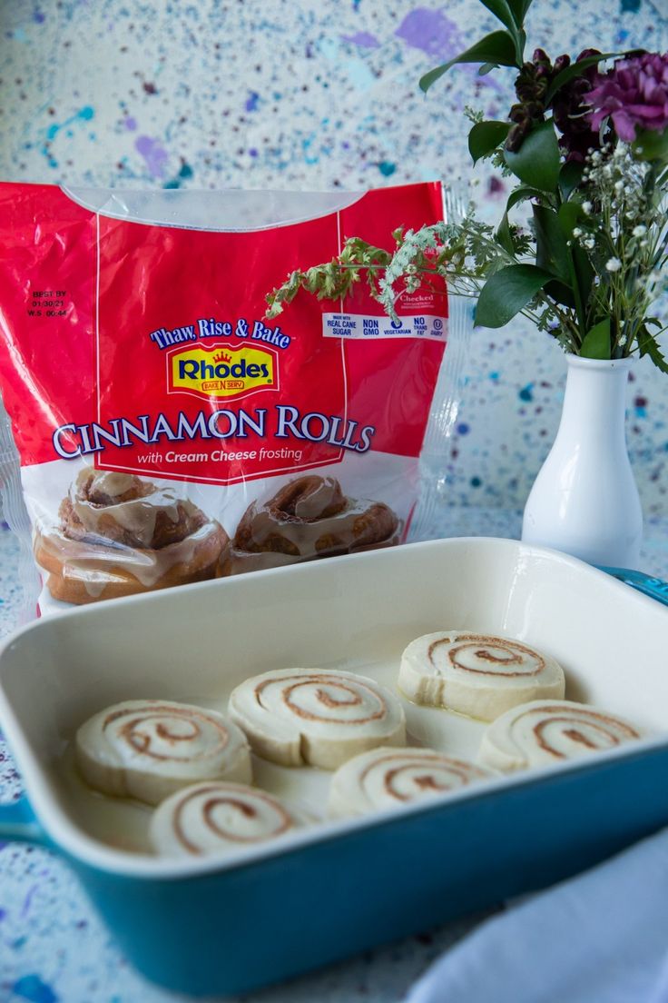 cinnamon rolls in a baking dish next to a bouquet of flowers and a bag of chips