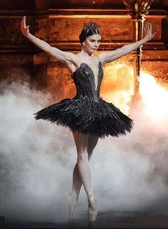 a ballerina in a black tutu and feathered dress with her arms outstretched