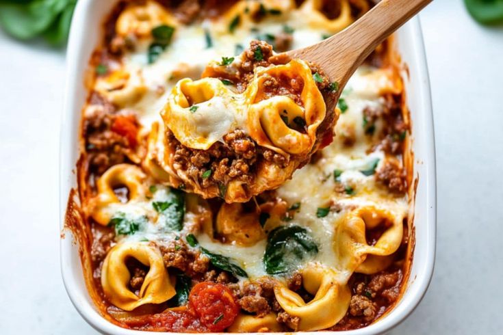 a casserole dish with meat, cheese and spinach is being held up by a wooden spoon