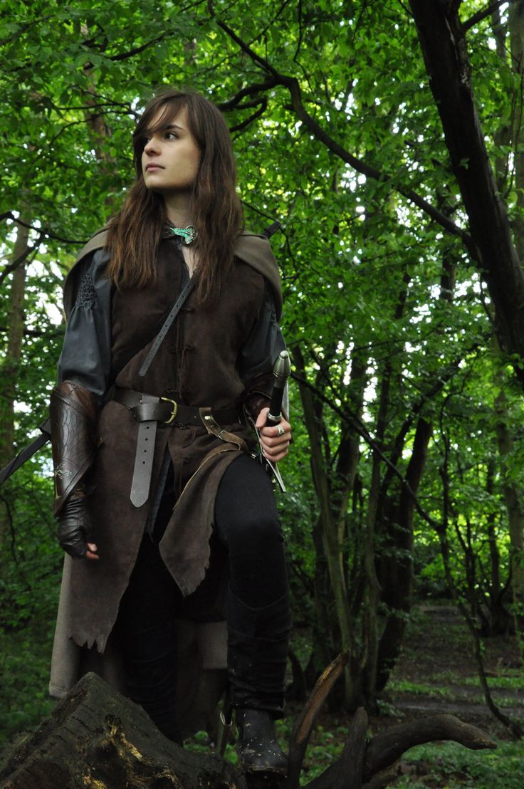 a woman dressed in medieval clothing stands on a rock and looks off into the distance