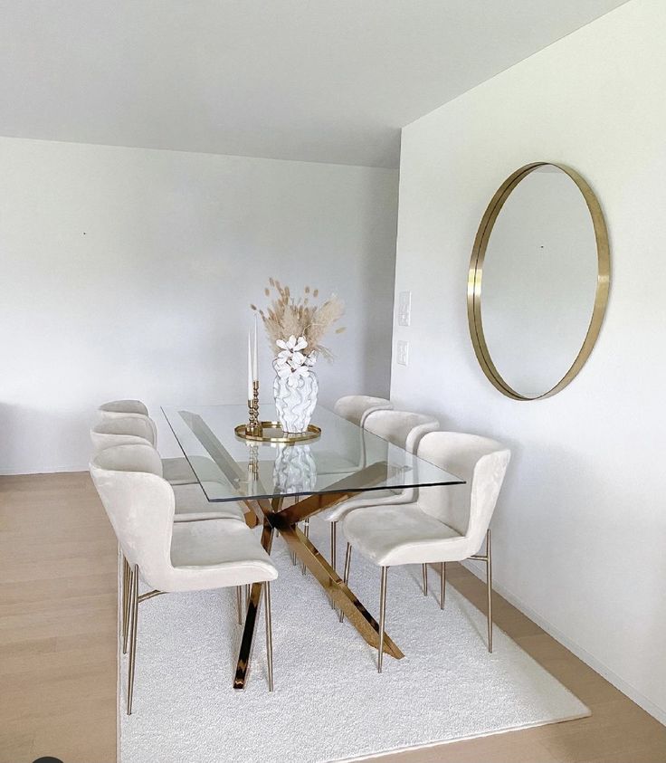 a glass dining table with white chairs and a round mirror on the wall above it