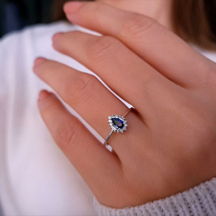 a woman's hand wearing a diamond and blue sapphire engagement ring on her finger