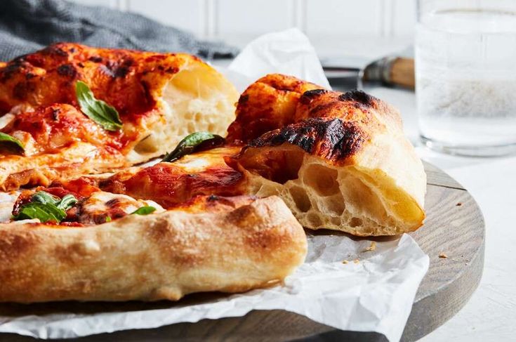 a pizza sitting on top of a wooden cutting board next to a glass of water