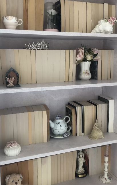 coquette white bookcase with antiques / china and flowers  on it Coquette Bookshelf Aesthetic, Coquette Book Shelf, Coquette Shelf Decor, Coquette Shelves, Vintage Book Shelf Aesthetic, Octavia Aesthetic, White Bookshelf Aesthetic, Coquette Library, Coquette Shelf