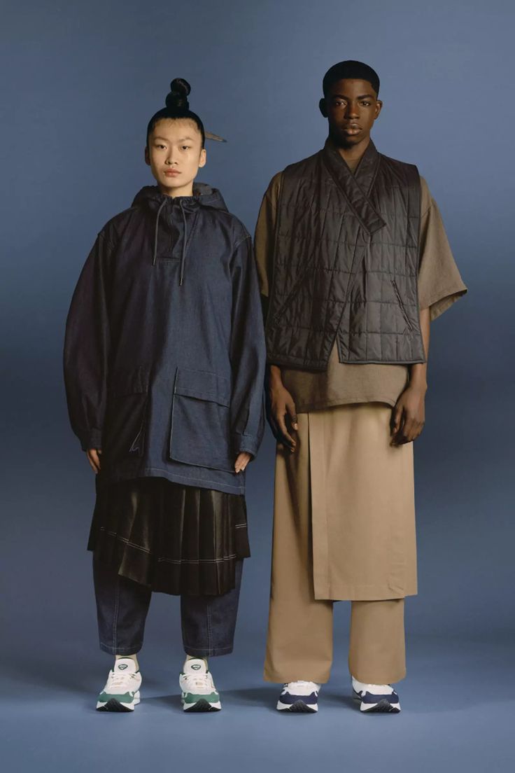 two young men standing next to each other in front of a blue background, one wearing an oversize jacket