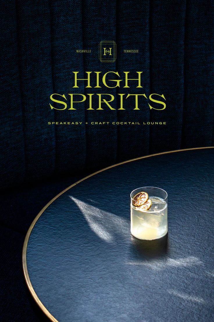 a drink sitting on top of a table next to a black wall with the words high spirits