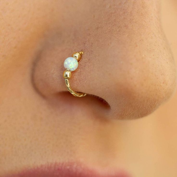 a woman's nose with a gold nose ring and white opal bead