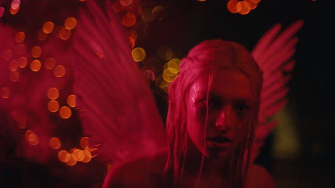 a woman with pink hair and angel wings standing in front of bright boke lights