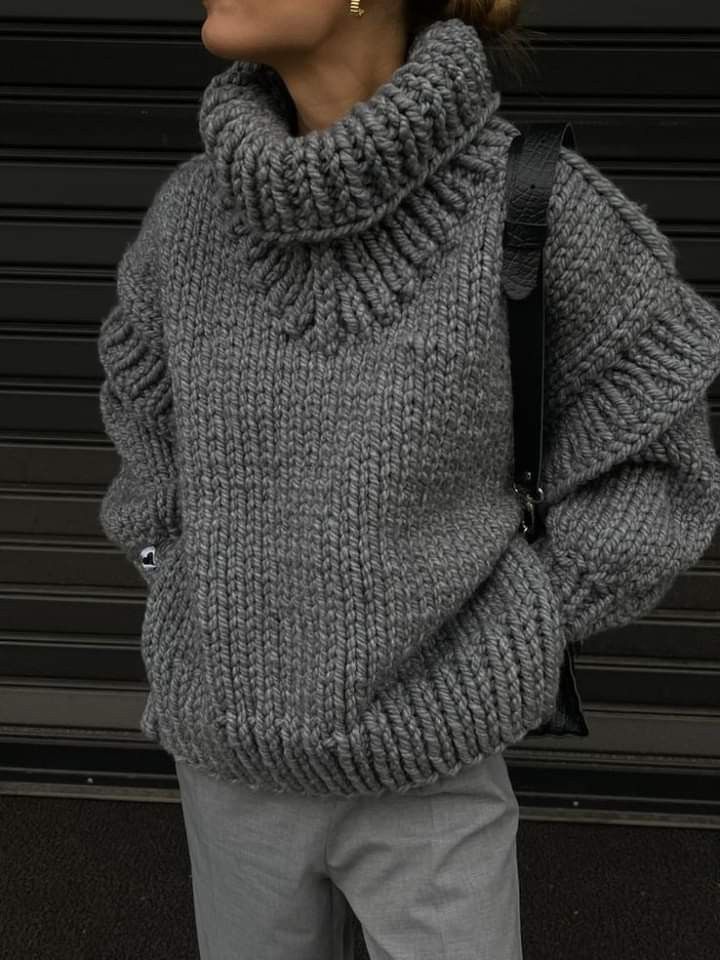 a woman wearing a gray sweater and grey pants is standing in front of a garage door