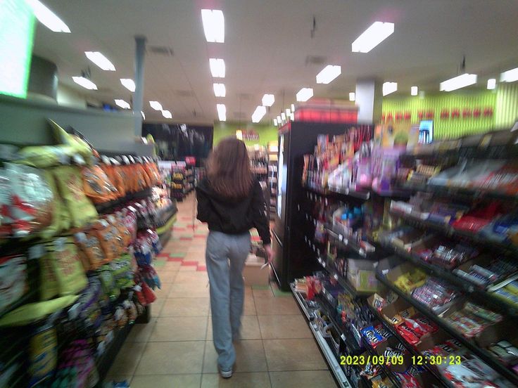 a blurry photo of a woman walking down a aisle in a grocery store with lots of items