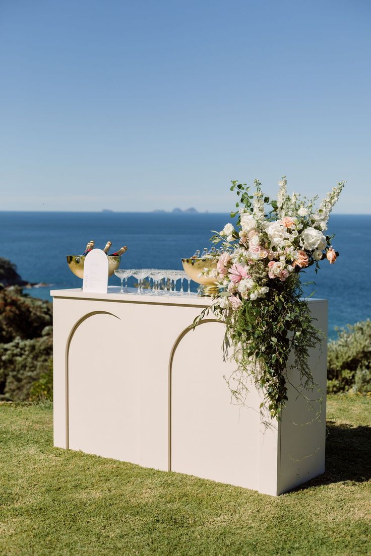 an outdoor ceremony setup with flowers and greenery on the grass near the water's edge