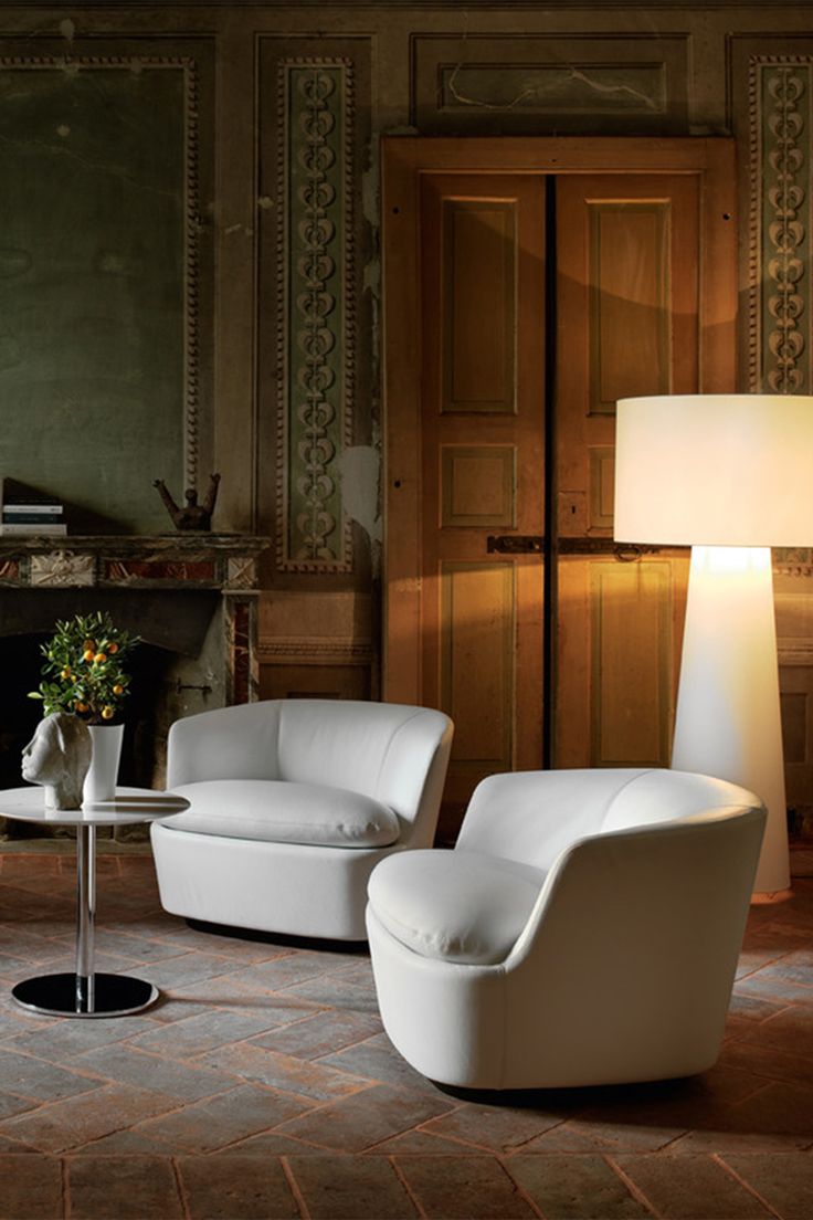 a living room with two chairs and a table in front of a fire place on the wall