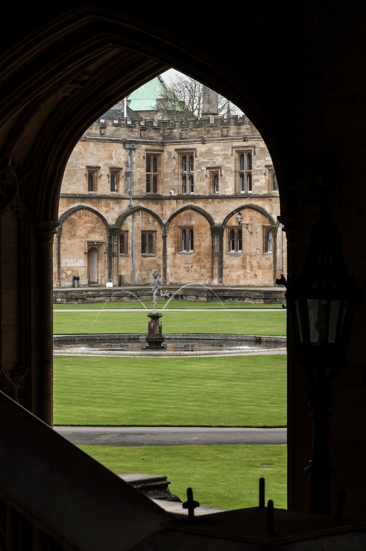 an archway leading to a large building with a fountain in the foreground and grass on the other side