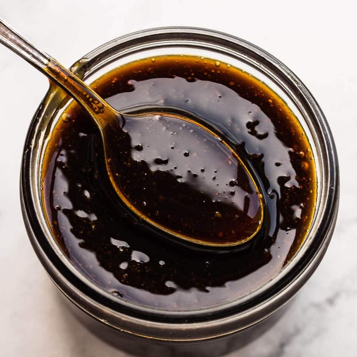 a glass jar filled with brown liquid on top of a white countertop next to a spoon