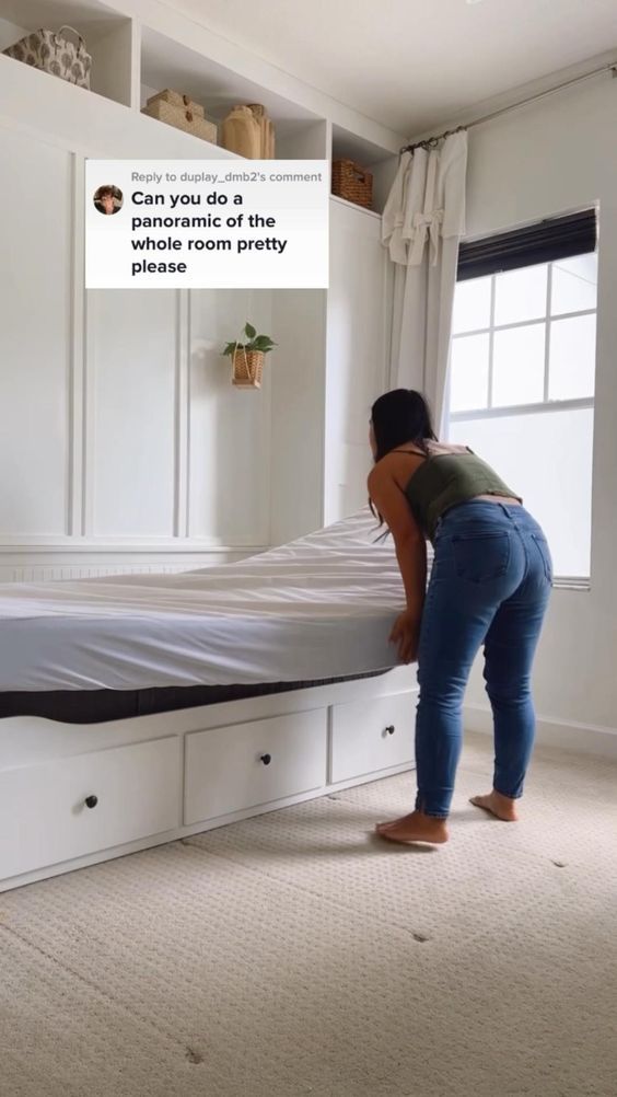 a woman standing over a bed in a room with white walls and carpeted floors