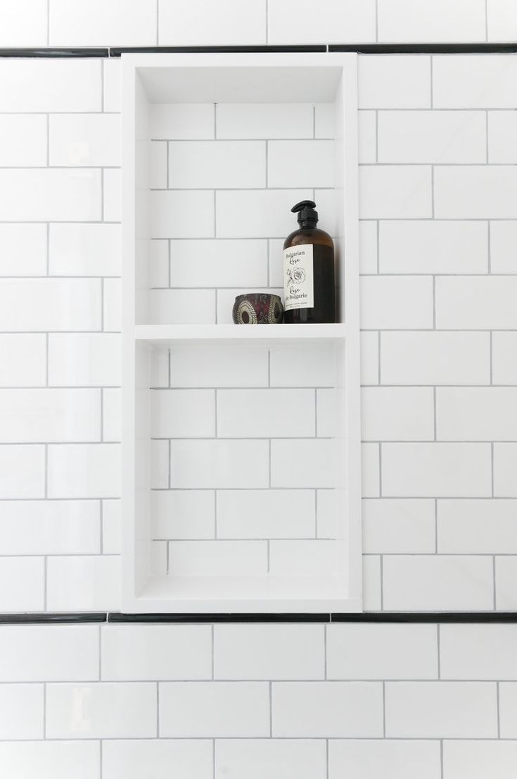 a white shelf with some bottles on top of it next to a tiled bathroom wall