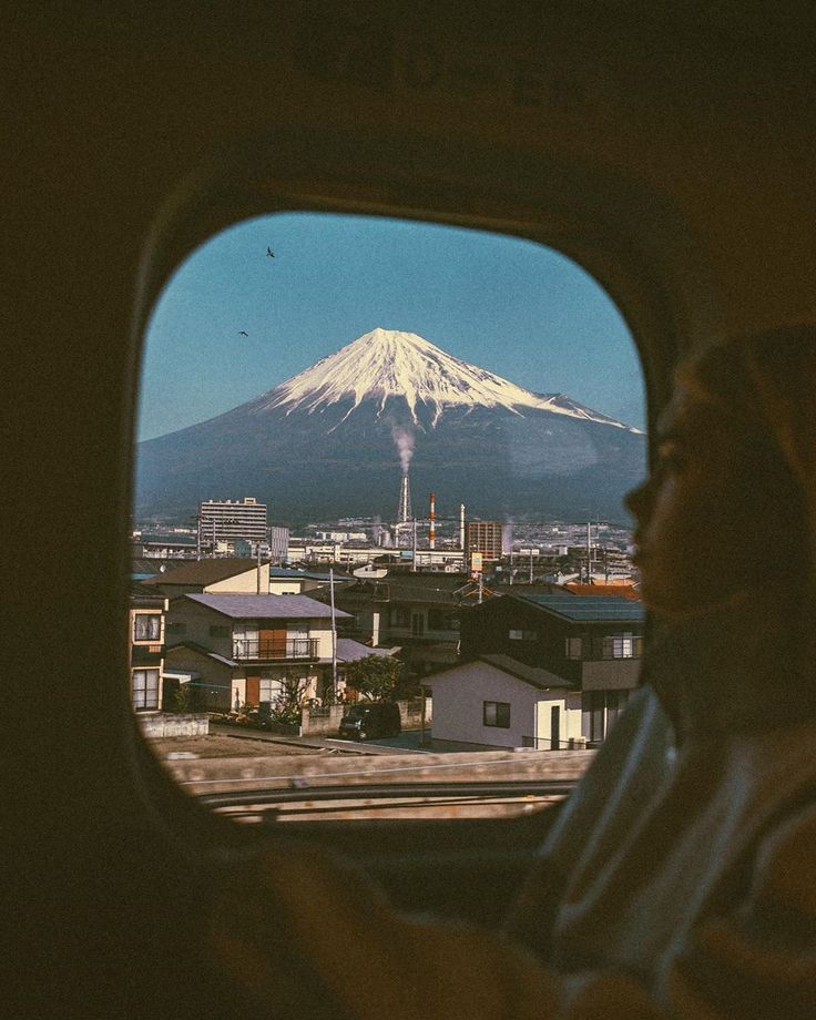 a woman looking out the window of an airplane at a snow covered mountain in the distance