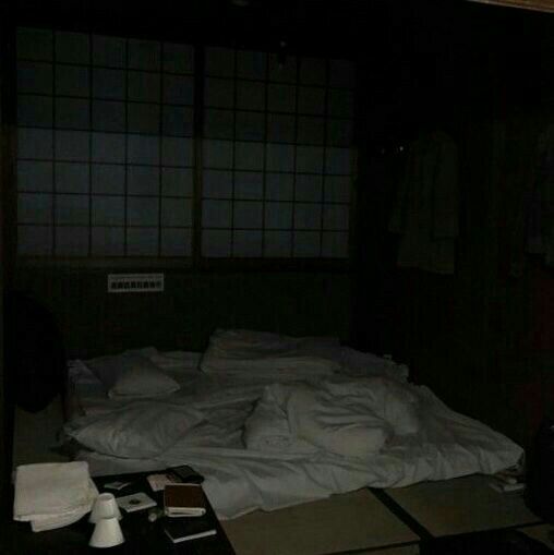 an unmade bed in a dark room with white sheets and pillows on the floor