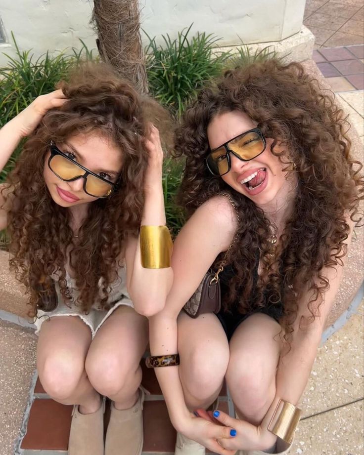 two young women sitting next to each other with their hands on their hipss and wearing sunglasses