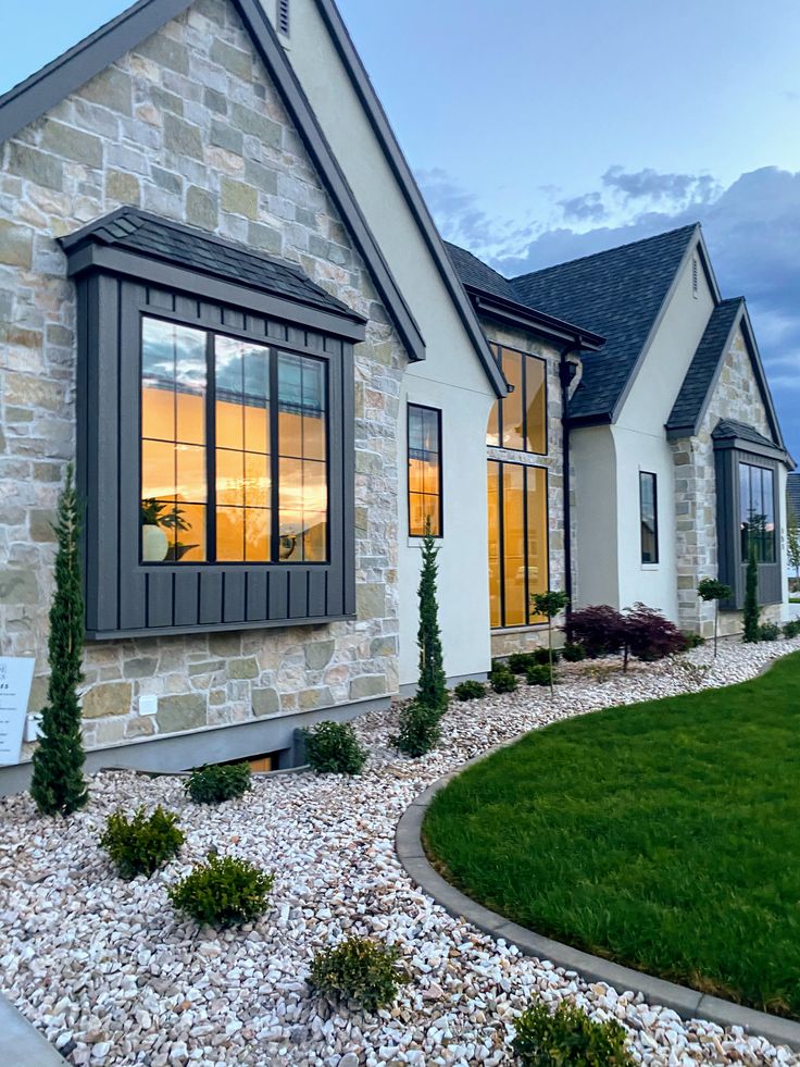 a house that is sitting in the middle of some rocks and grass with bushes around it