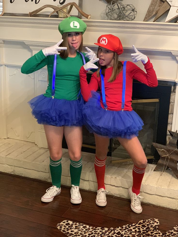 two women dressed up as mario and luigi in front of a fireplace with their hands on their hipss