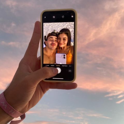 someone holding up their cell phone to take a selfie with the sky in the background