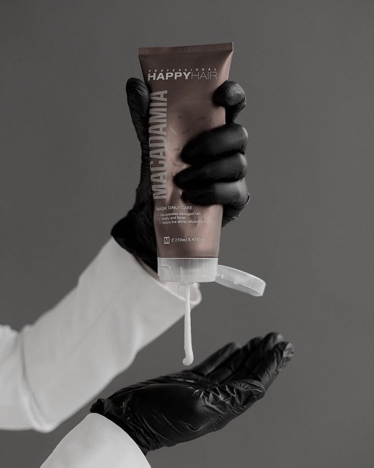 a person wearing black gloves and holding up a tube of toothpaste in their hand