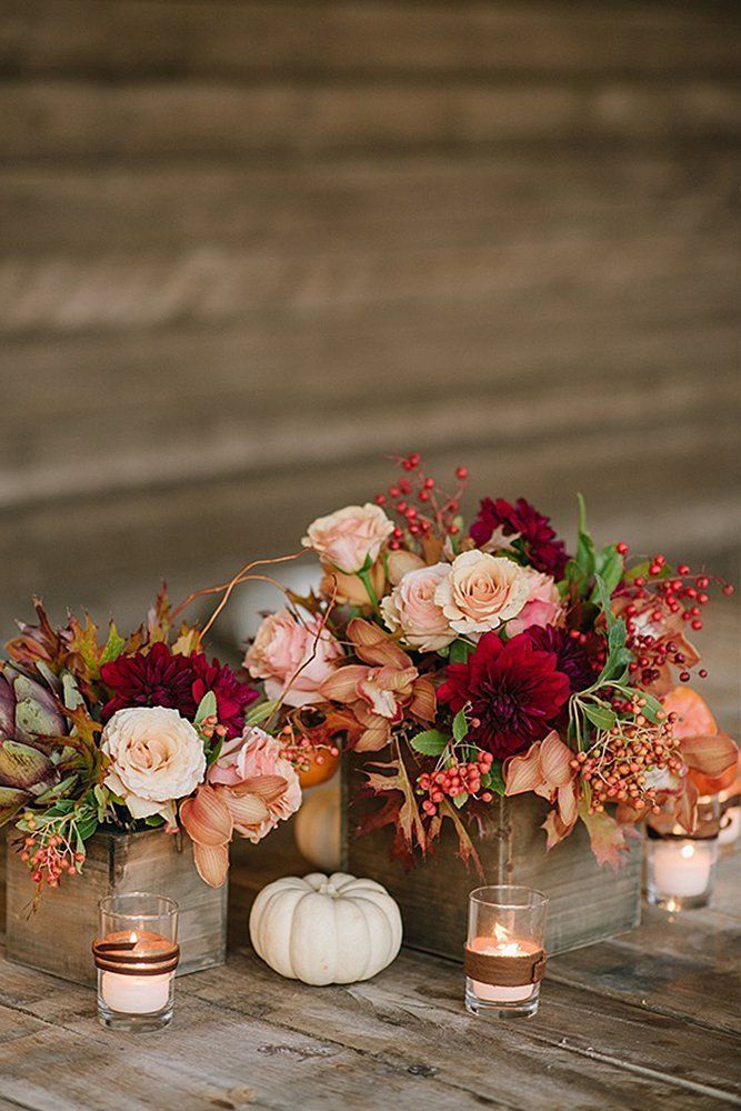 flowers and candles are arranged in vases on a wooden table with white pumpkins