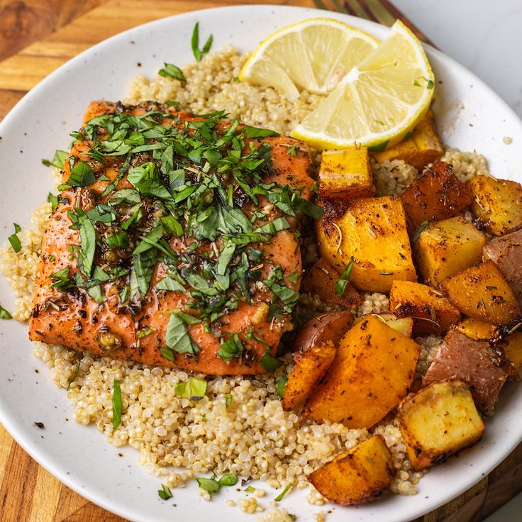 a white plate topped with salmon, potatoes and lemon wedges on top of couscous