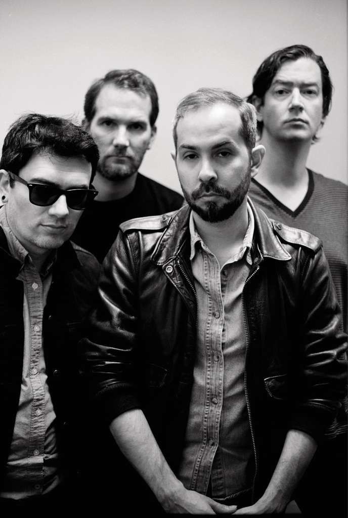 three men standing next to each other in front of a wall with one man wearing sunglasses