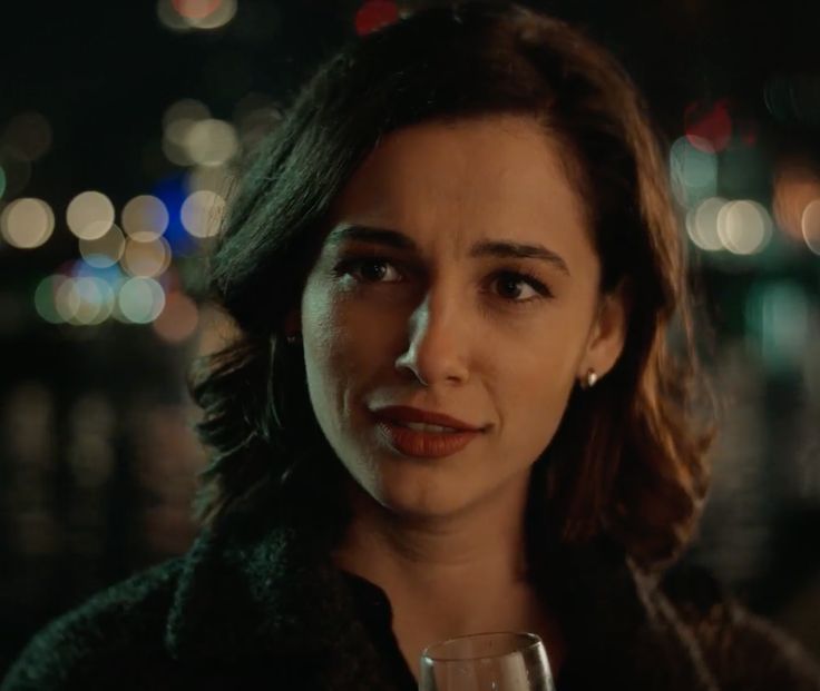 a woman holding a wine glass in front of a cityscape at night time