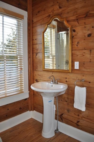 a bathroom with wood paneling and a white pedestal sink under a mirror on the wall