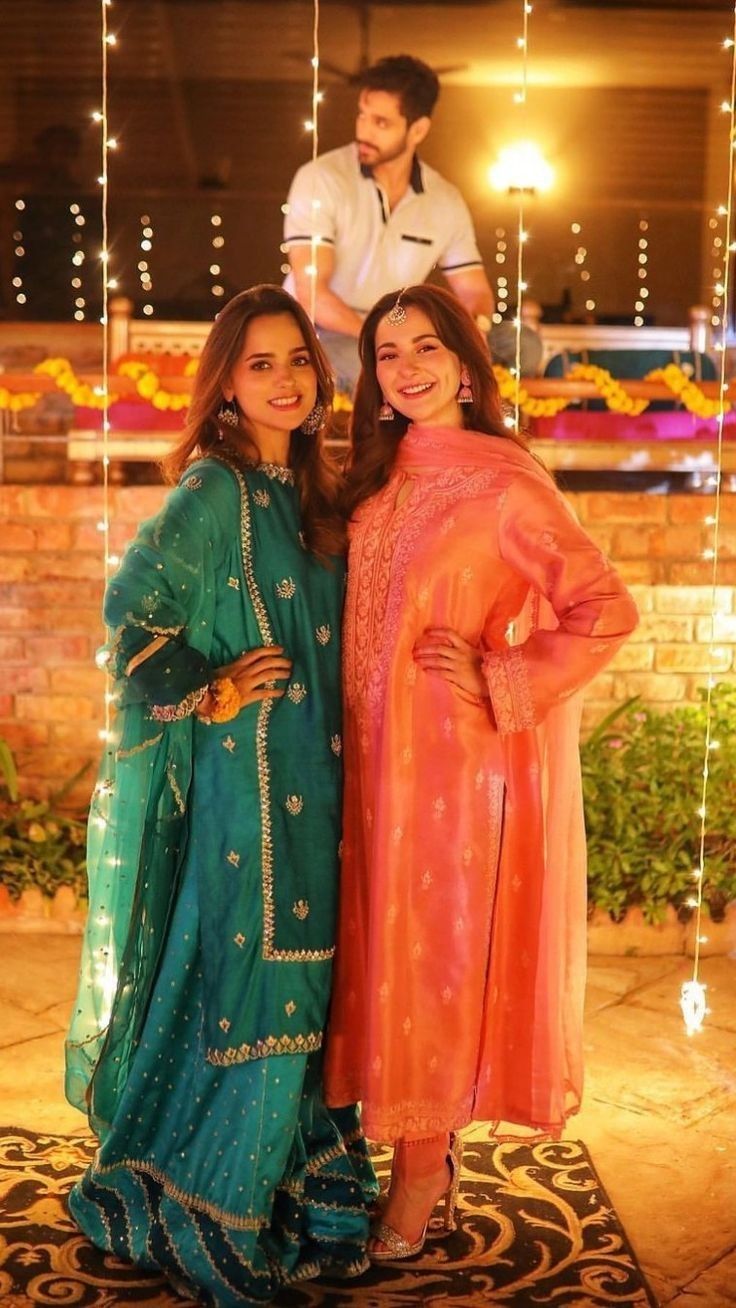 two women standing next to each other in front of some string lights and garlands