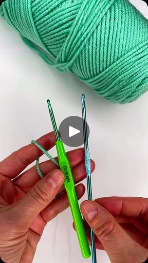 two hands holding green yarn and crochet hooks next to a ball of thread