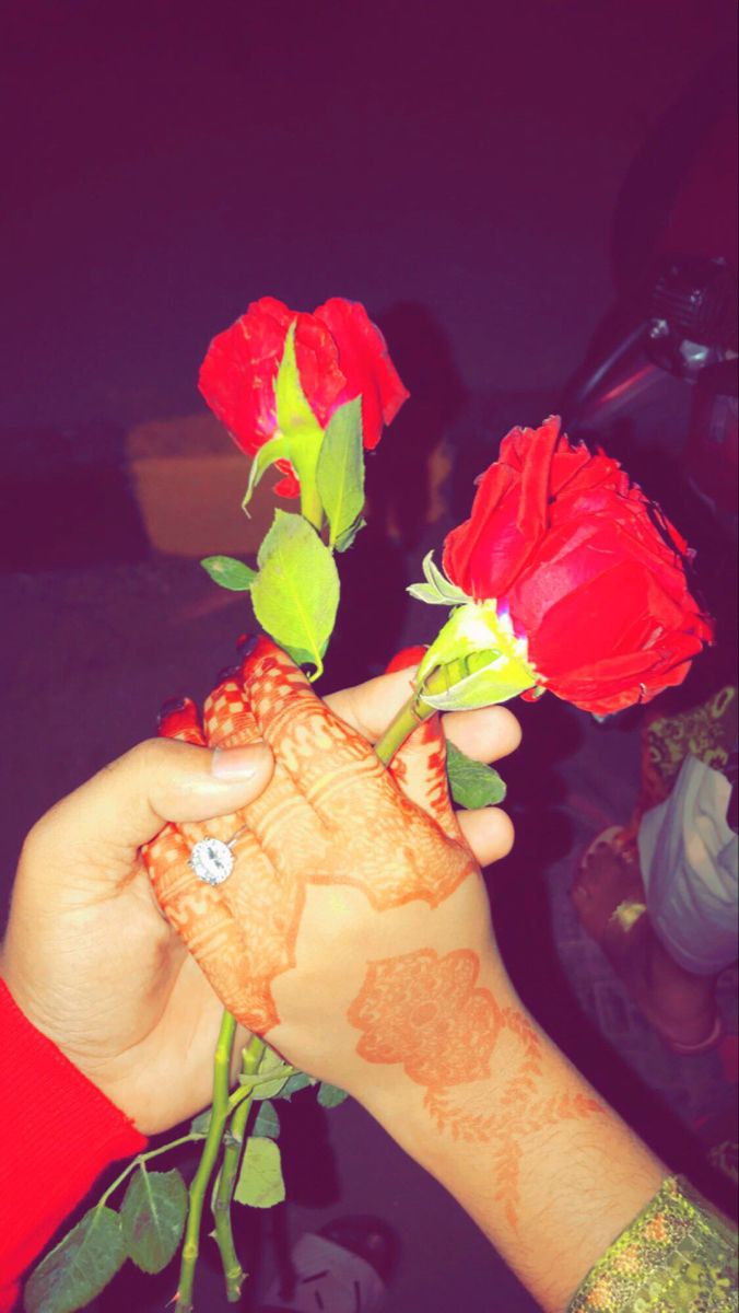 a woman's hand holding three roses with henna on her left and right arm