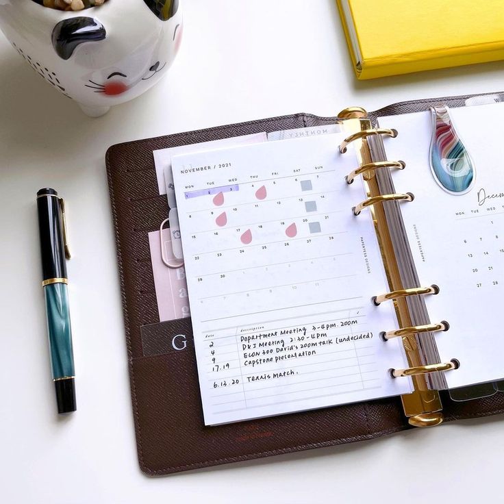 an open planner book next to a cup of coffee and a pen on a desk