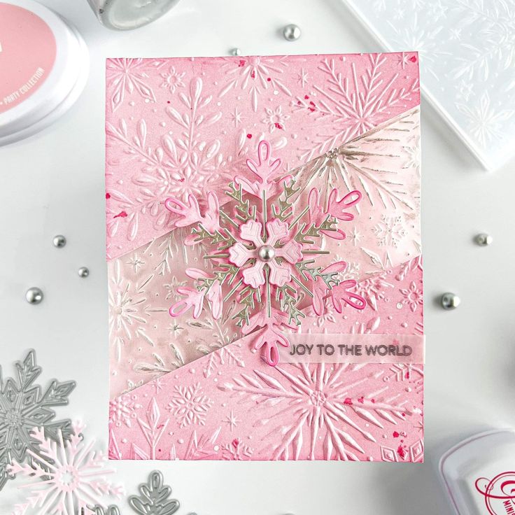 a pink card with snowflakes on it next to some silver and white decorations