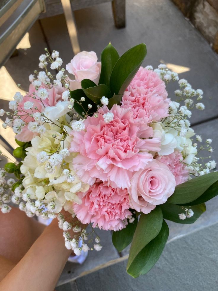 a bouquet of pink and white flowers sitting on top of a wooden bench next to a person's hand