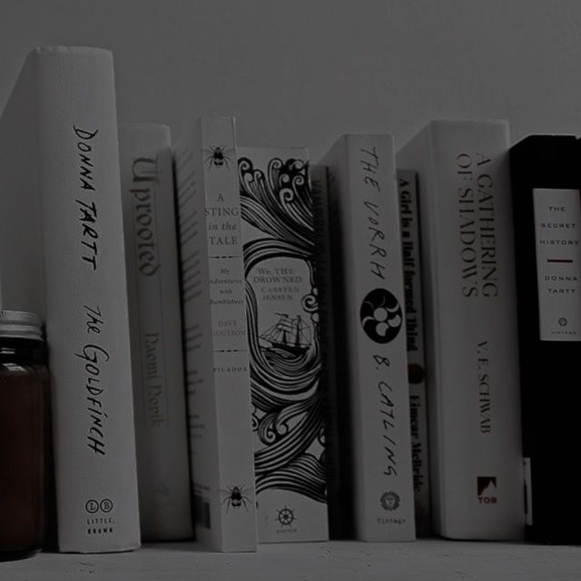 a row of books sitting on top of a white shelf next to a black bottle