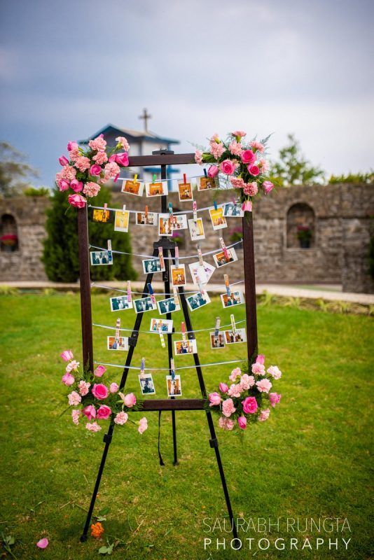 an easel with pictures and flowers on it in the grass next to a building