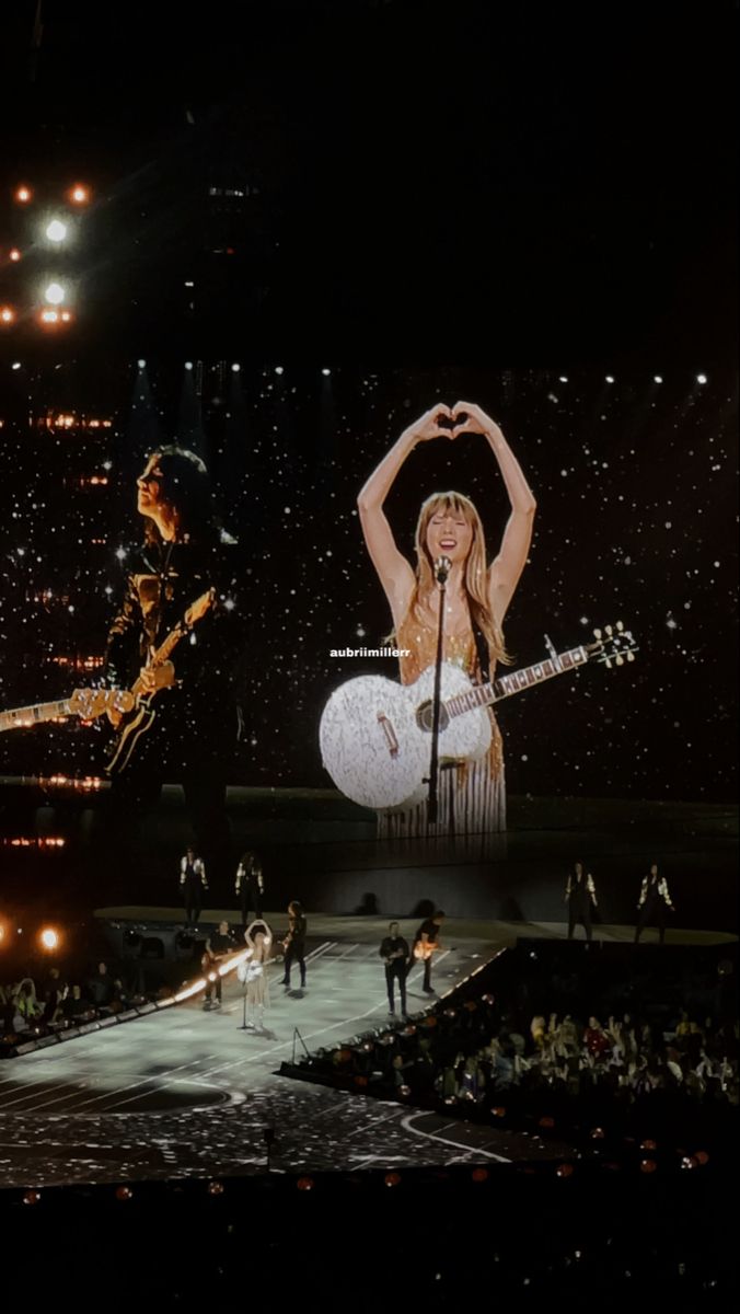 two women on stage with guitars and one holding her hands up in the air as she sings