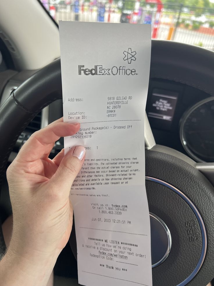 a person holding up a receipt in their hand next to the steering wheel of a car