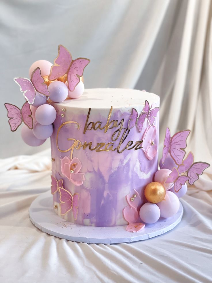 there is a purple cake with pink butterflies on the top and gold decorations around it