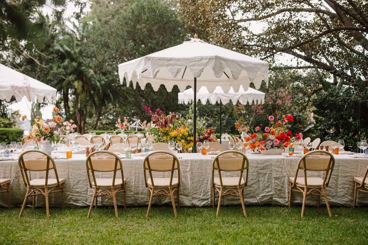 an outdoor table set up with chairs and tables covered in white linens, surrounded by flowers